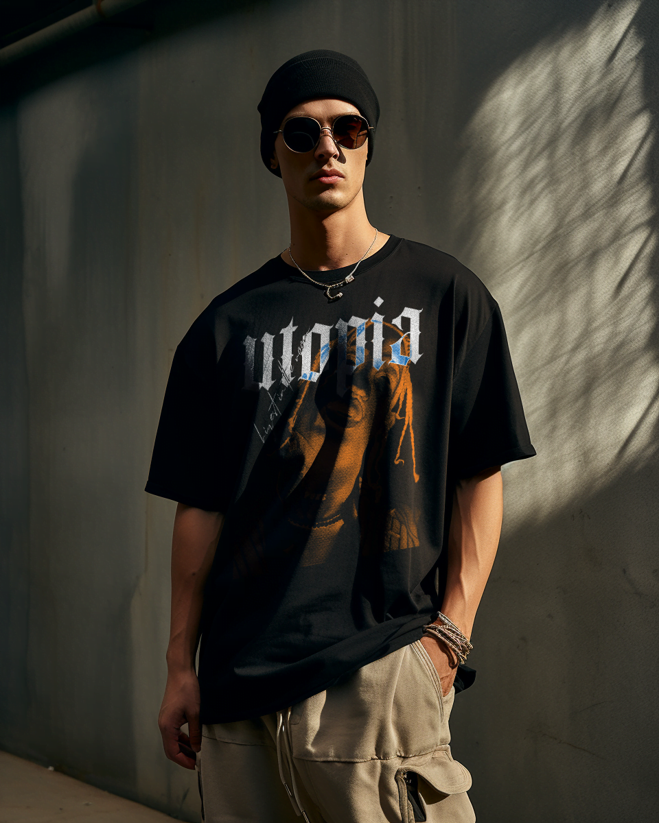 Man wearing Hiyest oversized black streetwear t-shirt with Utopia Travis Scott print, paired with beige olive cargos, black beanie, and sunglasses, in a grungy cement warehouse, Directional Sunlight.